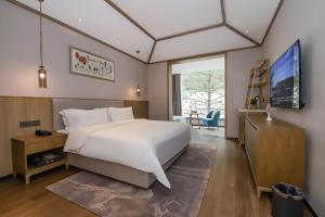 1 dormitorio con 1 cama blanca grande y TV en Qianhe International Hotel, en Jiuzhaigou