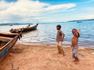two young boys standing on the beach near a boat at Home On The Nile Ernest Hemingway Suite in Jinja