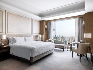 a bedroom with a bed and a chair and a large window at The Langham, Hefei in Hefei