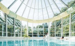 EurothermenResort Bad Hall - Hotel Miraverde في باد هول: رجل وامرأه يجلسون في المسبح في بيت زجاجي