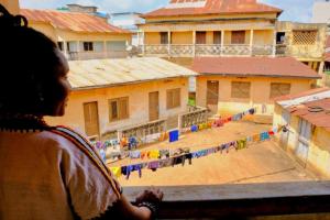 Ein junges Mädchen, das aus dem Fenster auf einen Innenhof blickt. in der Unterkunft Chambres d'hôtes - Chez Mama Sêdjro in Porto-Novo