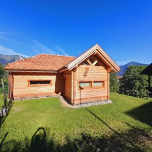 a wooden house with a grassy yard in front of it at Chalet Ridente con Patio al Gufo in Ovaro