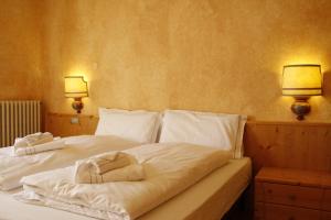 1 cama con sábanas blancas y 2 lámparas en la pared en Villa Ginestra - 1, en Moena