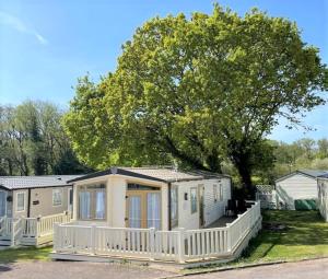 a small house with a white porch and a tree at Sea Breeze a beautiful 3 bedroom coastal caravan in Milford on Sea