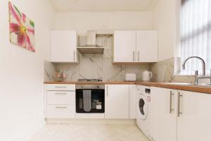 a kitchen with white cabinets and a washer and dryer at Dent House Stays in Hunslet
