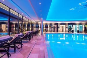 a swimming pool in a building with chairs and tables at Hotel EDELWEISS Berchtesgaden Superior in Berchtesgaden