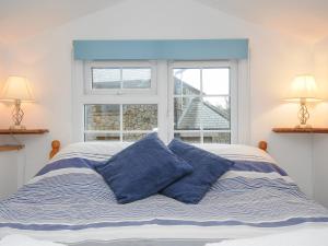 a bed with blue pillows in front of a window at Mole Cottage in Liskeard