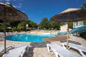 a swimming pool with white chairs and umbrellas at Camping le Clou in Coux-et-Bigaroque
