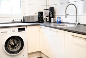 eine weiße Küche mit einer Waschmaschine und einem Waschbecken in der Unterkunft TRUTH für 5 - King Size Betten, Kamin, Garten, XXL Couch, Smart-TV in Dortmund