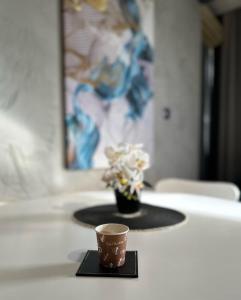 a coffee cup on a table with a vase of flowers at MT Apartments Skopje in Skopje