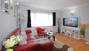 a living room with a red couch and a tv at Cheerful 3 Bedroom 2 Bathroom Bungalow by CozyNest in Earley
