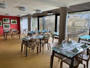 uma sala de jantar com mesas, cadeiras e janelas em Hôtel du Musée de l'Eau em Pont-en-Royans