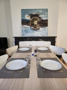 una mesa de comedor con platos blancos y una pintura en Agréable appartement, lumineux, en Bar-le-Duc