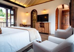 a bedroom with a bed and two chairs and a television at Hotel Casa Alcestre in Villa de Leyva