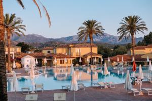 un hotel con piscina con sillas y palmeras en Valtur Baia dei Pini, en Budoni