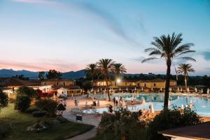 a resort with a large swimming pool with palm trees at Valtur Baia dei Pini in Budoni