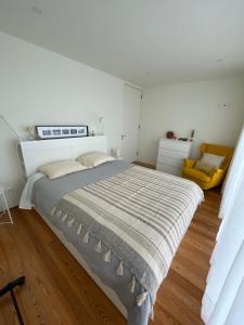 a white bedroom with a bed and a yellow chair at Sea & Rocks 15 - House in Lagoa