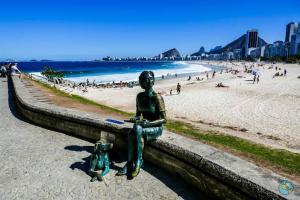 a statue of a woman sitting on a wall next to a beach at Praia mais charmosa do Rio in Rio de Janeiro