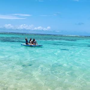 three people on a paddle board in the ocean at Panama Beachfront Apartments, Rarotonga in Rarotonga