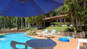 einen Tisch und Stühle mit einem Sonnenschirm neben einem Pool in der Unterkunft Casa de Campo em Ibiúna de frente para represa in Ibiúna