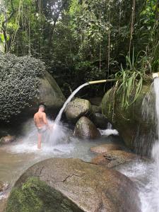 een man staat in een rivier onder een waterval bij Pousada Korui in Abraão