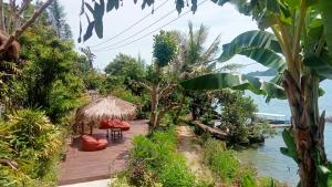 una terraza de madera con sillas y una cabaña junto al agua en Tanjungan, en Gili Gede