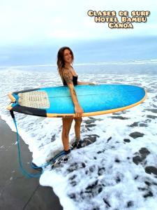 a woman standing on the beach holding a surfboard at Hotel Bambú in Canoa