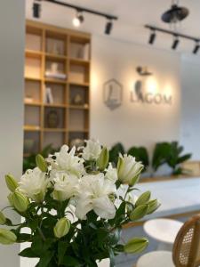 LAGOM APARTMENT AND HOTEL في دا نانغ: مزهرية من الزهور البيضاء تقف على طاولة