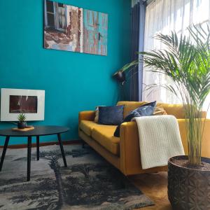a living room with a yellow couch and a blue wall at Feel at Home - Holiday Studio in Gulpen