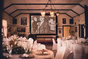 a room with white tables and white chairs and a large screen at Green Lantern Inn in Van Reenen