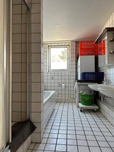a bathroom with a white tiled floor and a tub and sink at WinWin im Westen in Bielefeld