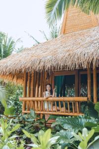 a woman sitting on a porch of a thatch hut at Phi Phi CoCo Beach Resort - SHA Extra Plus in Phi Phi Islands