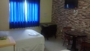 Hotel Dois Candangos في برازيليا: غرفة بسرير وطاولة وستائر زرقاء
