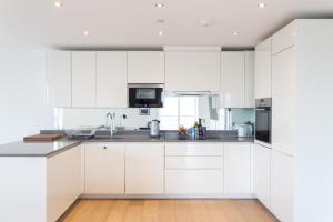 a white kitchen with white cabinets and a wooden floor at 2 Bed 2 Bath Penthouse With Amazing Views with Free Parking in London