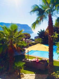 a pool with palm trees and a person laying on a couch and an umbrella at Astoria Villa maison d hôtes Appartement vue mer avec piscine in Cassis