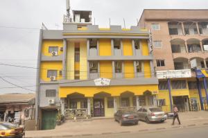 un bâtiment jaune avec des voitures garées devant lui dans l'établissement HOTEL DE LA VALLEE NEW, à Yaoundé