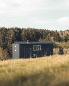 a black building in the middle of a field at Dog friendly Beautifully furnished Shepherds Hut set in the Kent Countryside in Aldington