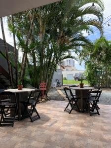 two tables and chairs on a patio with palm trees at Fica, Vai ter Bolo Hostel in Itajaí