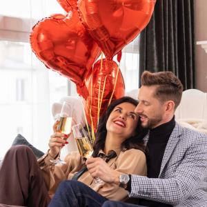 un homme et une femme assis sur un canapé avec ballons et verres à vin dans l'établissement Paris j'Adore Hotel & Spa, à Paris