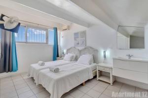 a white bedroom with two beds and a sink at Bonaire Oceanfront Apartments in Kralendijk