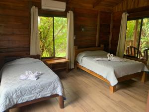 two beds in a room with wooden walls and windows at Cataratas Bijagua Lodge, incluye tour autoguiado Bijagua Waterfalls Hike in Bijagua