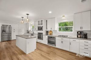 una cocina con armarios blancos y electrodomésticos de acero inoxidable en Capitol View 4k sqft Dwntwn Penthouse w 17ft Table, en Austin