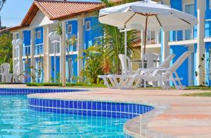 a resort with a swimming pool with chairs and an umbrella at DUPLEX 2 SUÍTES MONT SIÃO in Porto Seguro