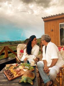 a man and woman sitting on a deck with a table of food at Refúgio Serra da Tartaruga - Alfredo Wagner in Alfredo Wagner