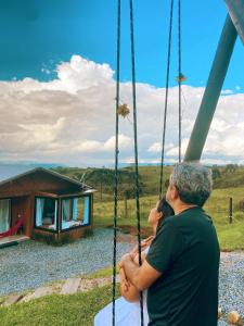 a man and woman sitting on a swing in front of a cabin at Refúgio Serra da Tartaruga - Alfredo Wagner in Alfredo Wagner
