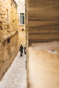 a man walking down a street in an alley at Palazzo Bifora in Mdina