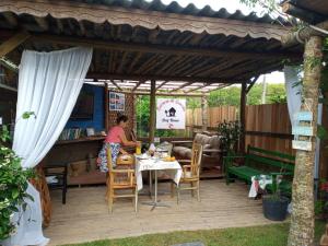 Eine Frau, die an einem Tisch unter einer Pergola sitzt. in der Unterkunft Essência da Guarda Surf House in Guarda do Embaú