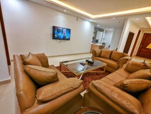 a living room with brown leather furniture and a tv at Sun-Rise view Luxury apartment Gold Crest Mall in Lahore