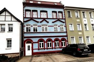 niebiesko-czerwony budynek z samochodem zaparkowanym przed nim w obiekcie Apartment für bis zu 7 Personen mit Balkon w mieście Halberstadt