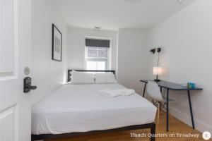 a white bedroom with a bed and a desk at West Broadway Quarters by Thatch in Boston